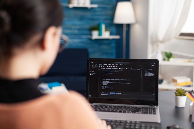 Young developer programming software typing html code deloping application for mobile use. Student working at infographics javascript using laptop computer while sitting at desk in living room