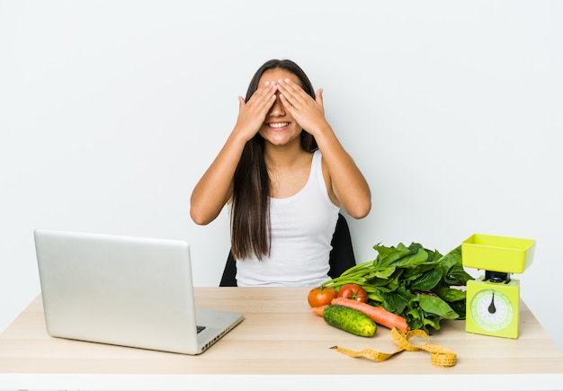 Young dietician asian woman covers eyes with hands, smiles broadly waiting for a surprise.