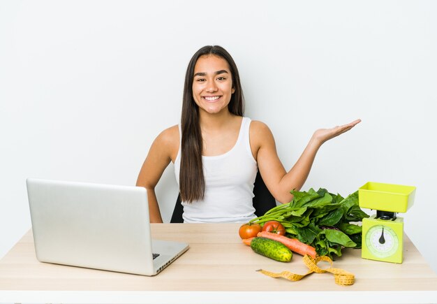 Young dietician asian woman isolated on white showing a copy space on a palm and holding another hand on waist.