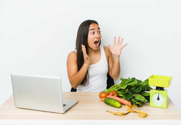 Young dietician asian woman isolated on white wall shouts loud, keeps eyes opened and hands tense.