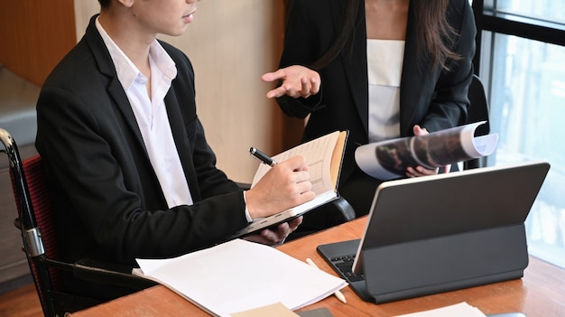 Young disabled male worker in wheelchair working with his colleague in office.