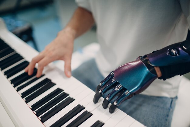 Young disabled man playing on piano electronic synthesizer with artificial prosthetic hand in music ...