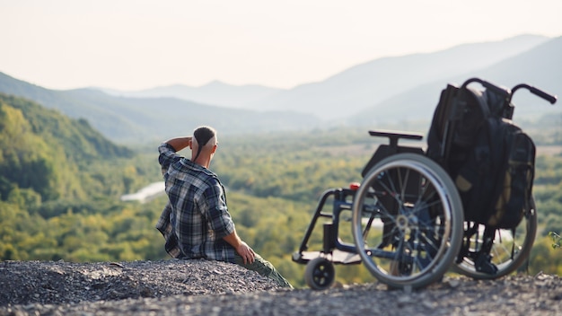 사진 젊은 장애인 휠체어 근처 산 정상에 앉아 신선한 공기와 자연의 아름다움을 즐기고 있습니다. 인생을 즐기고 있습니다.
