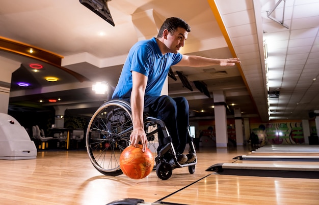 Young disabled man in wheelchair playing bowling in the club