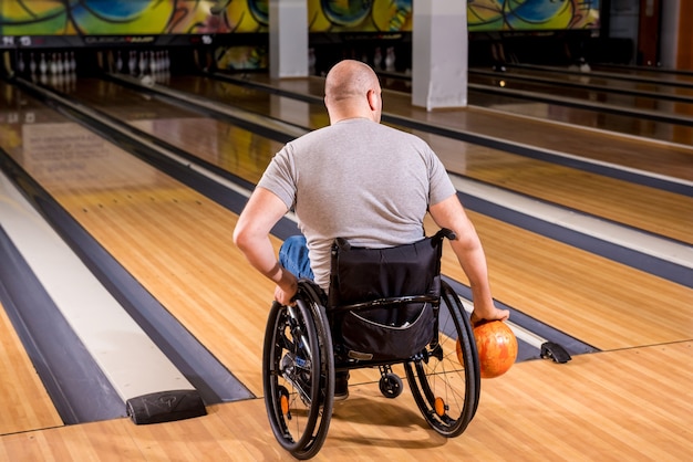 Young disabled man in wheelchair playing bowling in the club