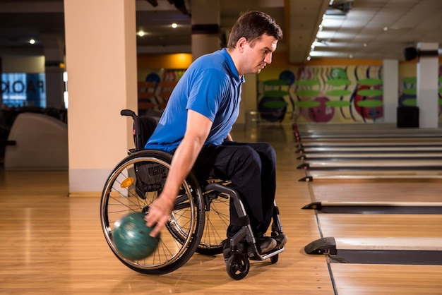 Молодой инвалид в инвалидной коляске, играя в боулинг в клубе