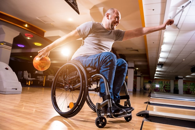 Young disabled man in wheelchair playing bowling in the club