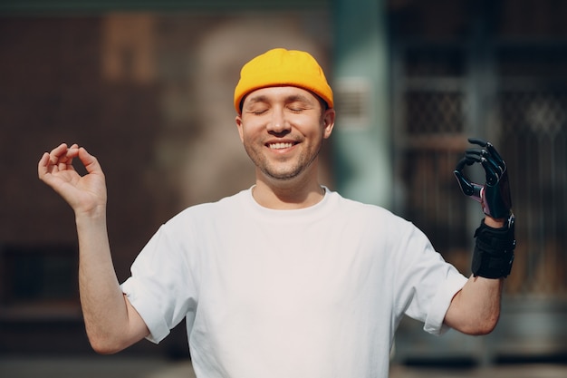 Young disabled man with artificial prosthetic hand ok gesture mudra meditate on city street outdoor