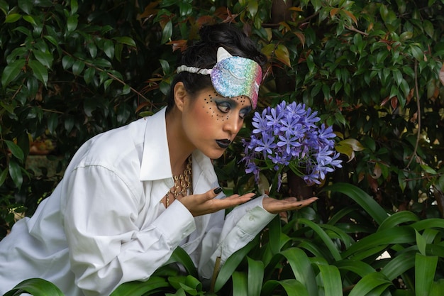 Young disguised woman with make up and colorful mask over her head looking a blue flower