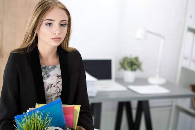 Young dismissed female worker in office holding carton box with her belongings. Getting fired concept.