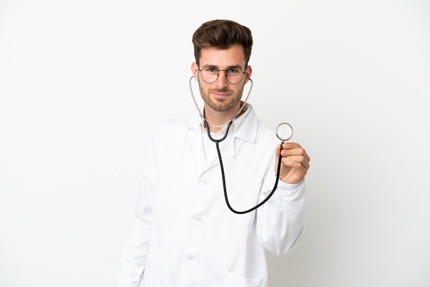 Young doctor caucasian man over isolated on white background wearing a doctor gown and with stethoscope