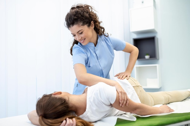 Young doctor chiropractor or osteopath fixing lying womans back with hands movements during visit in manual therapy clinic Professional chiropractor during work