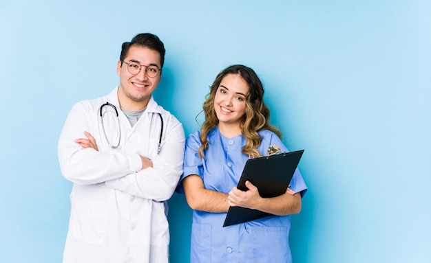 Young doctor couple posing in a blue wall isolated who feels confident, crossing arms with determination.