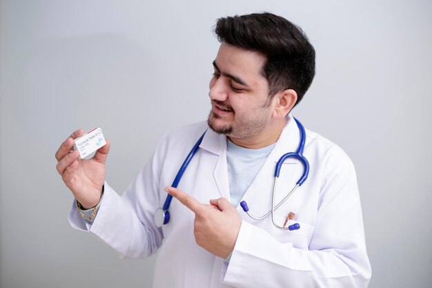 A young doctor is holding medicine in one hand and showing with finger