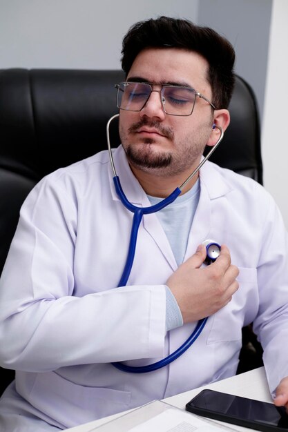 Photo a young doctor is sitting in the clinic checking his heartbeat with stethoscope