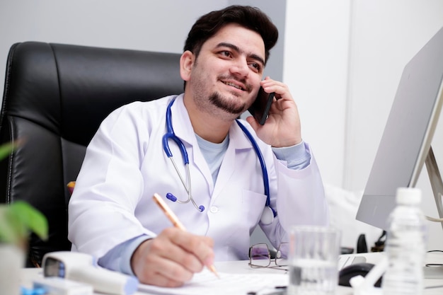 Foto un giovane medico è seduto in clinica e parla al cellulare