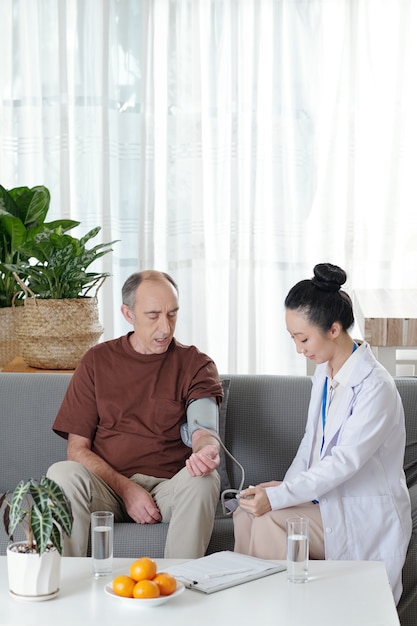 Young doctor looking at screen of electronic tonometer when measuring blood pressure of senior patient suffering from hypertension