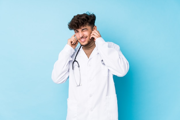 Young doctor man idolated covering ears with hands.