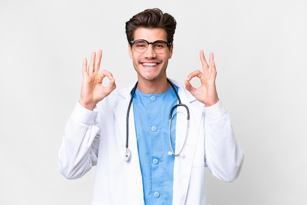 Young doctor man over isolated white background showing an ok sign with fingers