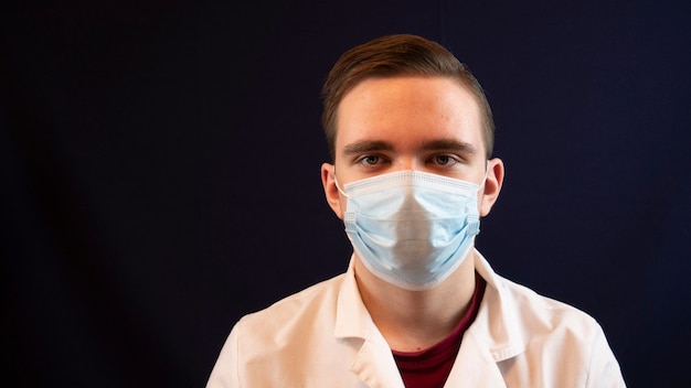 Young doctor, a man in a mask, in a white coat, close-up on a dark, looks at the patient's tests