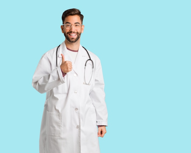 Young doctor man smiling and raising thumb up