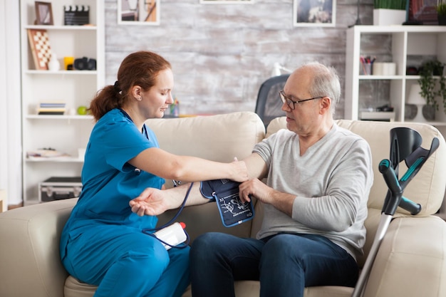 Foto giovane medico in casa di cura che prende la pressione sanguigna digitale del vecchio.