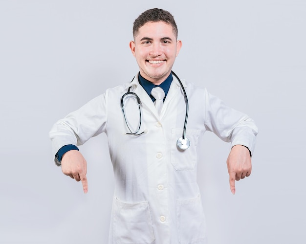 Young doctor pointing a promotion down Happy doctor pointing fingers down Latin doctor pointing down an isolated advertising space