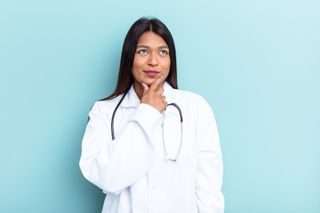 Young doctor Venezuelan woman isolated on blue background looking sideways with doubtful and skeptical expression.