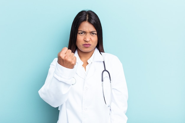 Young doctor Venezuelan woman isolated on blue background showing fist to camera, aggressive facial expression.