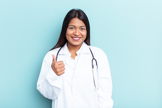 Young doctor Venezuelan woman isolated on blue background smiling and raising thumb up