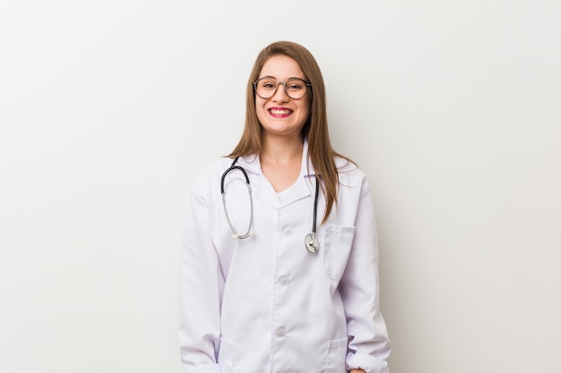 Young doctor woman against a white wall happy, smiling and cheerful.