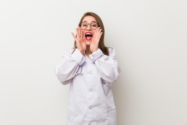 Young doctor woman against a white wall shouting excited front.