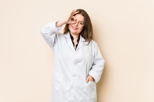 Young doctor woman excited keeping ok gesture on eye.