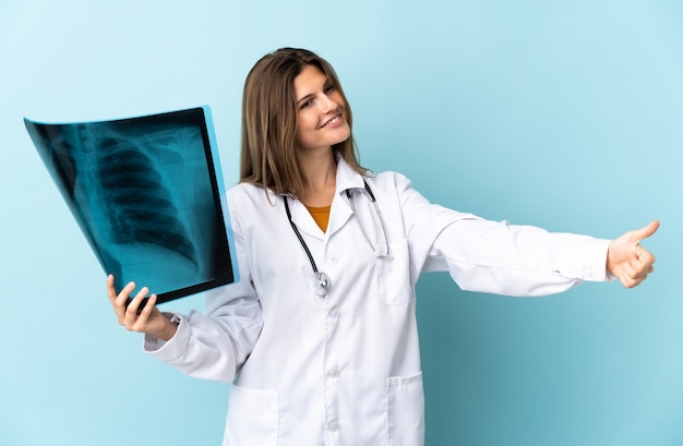 Young doctor woman holding radiography over isolated background giving a thumbs up gesture