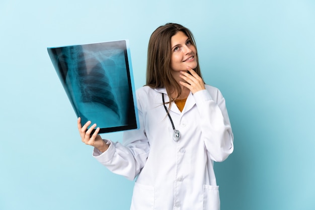 Young doctor woman holding radiography over isolated background looking up while smiling