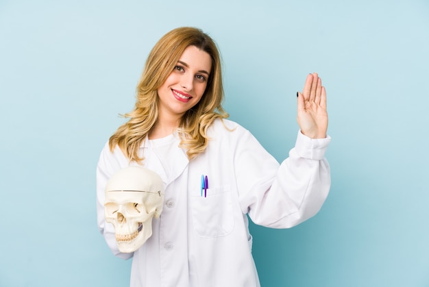 La giovane donna del medico che tiene un cranio ha isolato sorridente allegro che mostra il numero cinque con le dita.