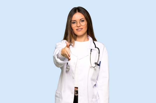 Giovane donna di medico che agita le mani per la chiusura del buon affare su fondo blu isolato