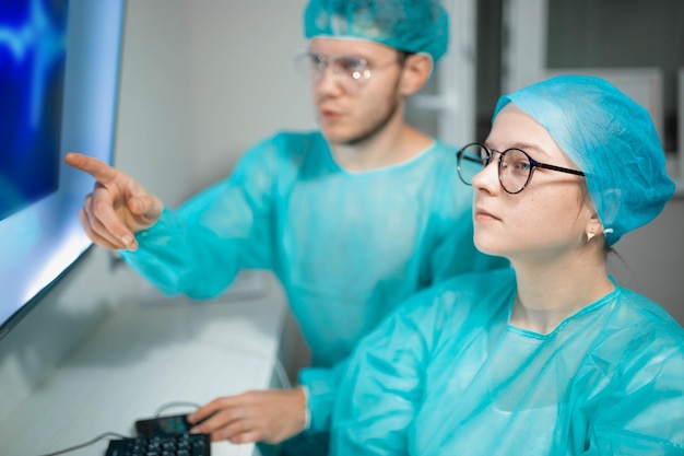 若い医師の同僚がコンピューターで働いて勉強している制服を着た男性と女性の外科医は研究者です