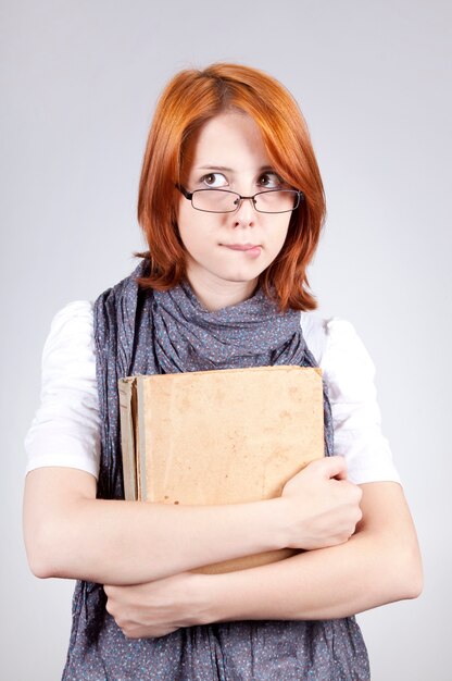 Giovane ragazza di moda dubbiosa in bicchieri con il vecchio libro