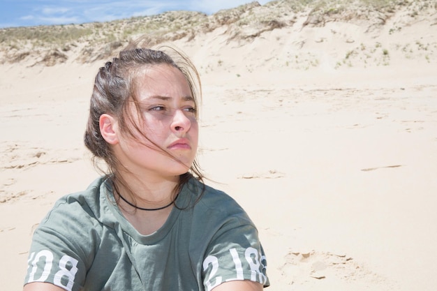 Young dreaming teenage girl with long dark hair sitting on dunes sandy beach