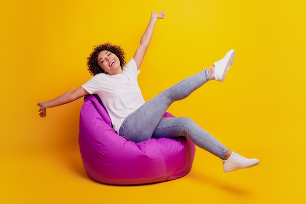 Young dreamy african girl sit beanbag rejoice celebrate victory on yellow background