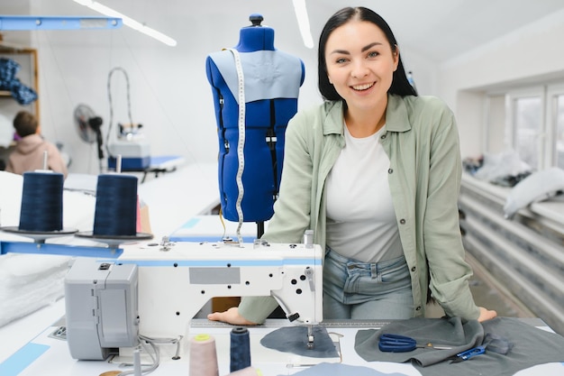 Young dressmaker woman sews clothes on working table Smiling seamstress and her hand close up in workshop