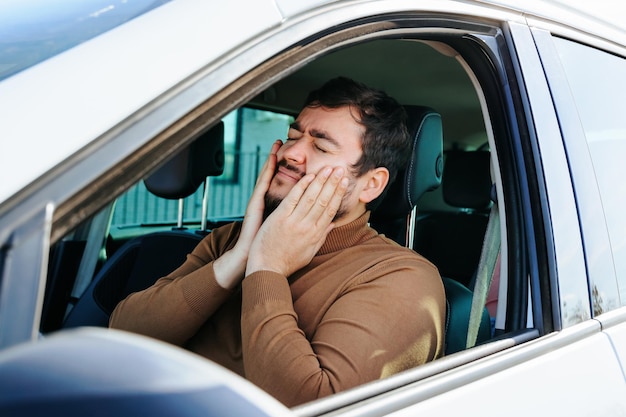 若い運転手は自分のを手で握っています彼の歯は車輪の後ろで多くの時間を痛めます