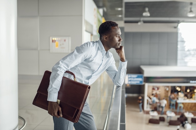 Young ebony businessman with briefcase looking on food-court. Successful business person in cafe, black man in formal wear