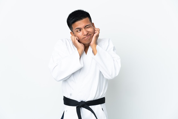 Young Ecuadorian man doing karate isolated on white wall frustrated and covering ears