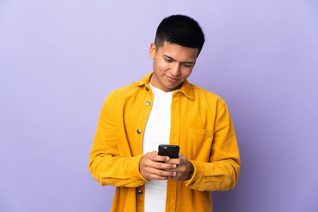 Young Ecuadorian man isolated on purple background sending a message with the mobile