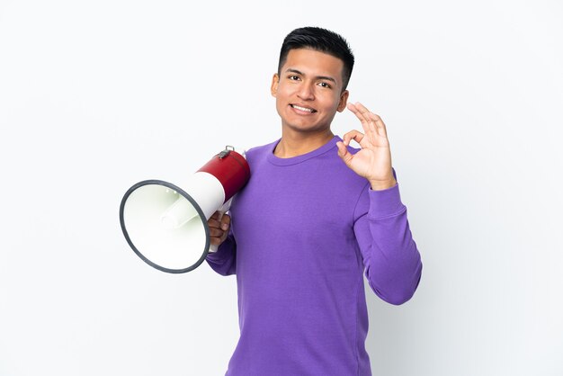 Young Ecuadorian man isolated on white background holding a megaphone and showing ok sign with fingers