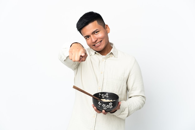Молодой эквадорский мужчина, изолированный на белой стене, с уверенным выражением лица указывает пальцем на вас, держа миску лапши с палочками для еды