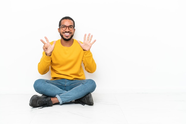 Young Ecuadorian man sitting on the floor isolated on white wall counting eight with fingers