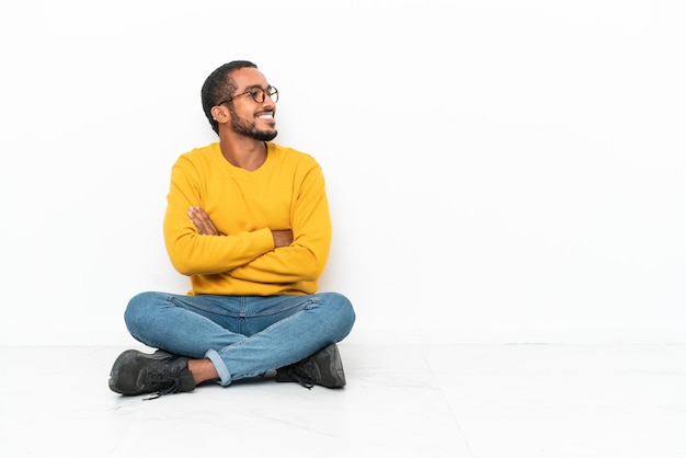 Young Ecuadorian man sitting on the floor isolated on white wall in lateral position